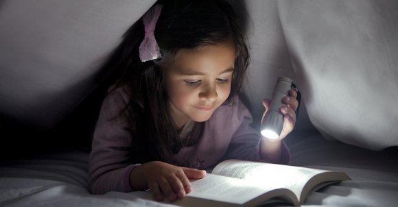 Little Girl Reading a Book in Bed and Using a Small Lantern