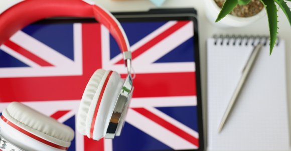 Tablet with image of British flag with headphones and notebook with pen lie on table. Learn British English remotely via app concept