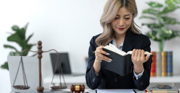 Attractive and confident Asian female lawyer working in the office with law books sitting at desk. Learn, study, legal services, advice, justice and real estate concept.